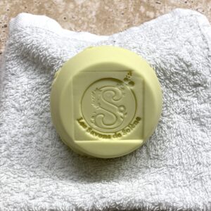 Shampoing solide rond blanc-crème posé sur une serviette blanche