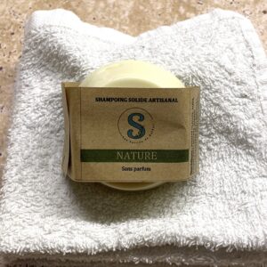 Shampoing solide rond blanc-crème emballé dans une étiquette kraft posé sur une serviette blanche