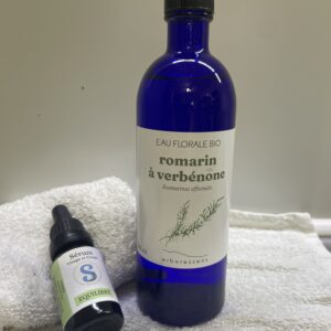 Bouteille bleu contenant de l'hydrolat de romarin a verbenone et flacon de sérum posé à côté