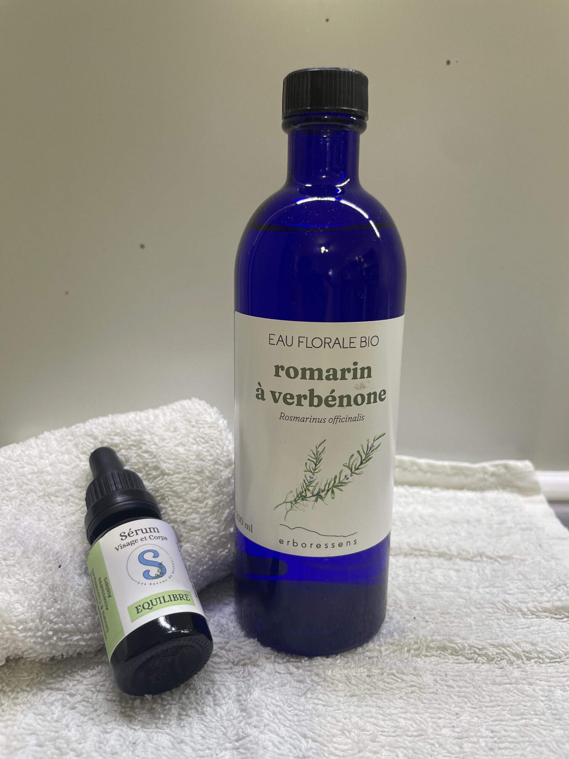 Bouteille bleu contenant de l'hydrolat de romarin a verbenone et flacon de sérum posé à côté
